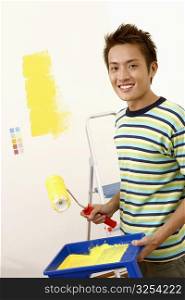 Portrait of a young man holding a paint roller with a paint tray and smiling
