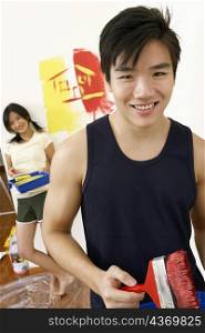 Portrait of a young man holding a paintbrush with a young woman standing in the background