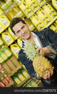 Portrait of a young man holding a pineapple in a supermarket