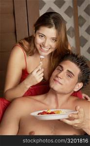 Portrait of a young man holding a plate of fruit salad with a young woman sitting behind him