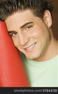 Portrait of a young man holding a rolled up exercise mat