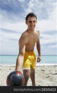 Portrait of a young man holding a soccer ball on the beach