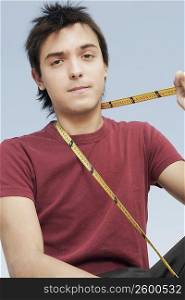 Portrait of a young man holding a tape measure around his neck