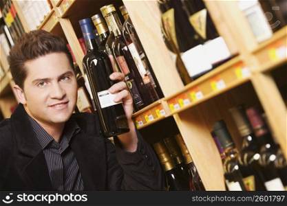Portrait of a young man holding a wine bottle in a liquor store