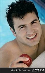 Portrait of a young man holding an apple in a swimming pool