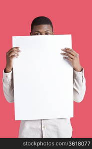 Portrait of a young man holding blank cardboard in front of face over pink background