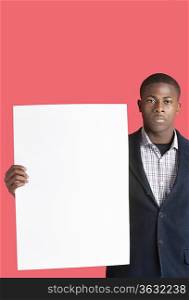 Portrait of a young man holding blank cardboard over pink background