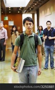 Portrait of a young man holding books with four people standing behind him in the corridor