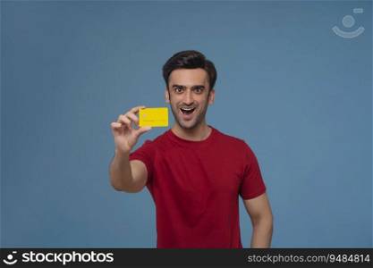 Portrait of a young man holding credit card in his hand against plain backdrop.