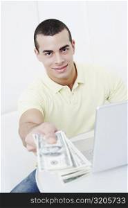 Portrait of a young man holding dollar bills in front of a laptop