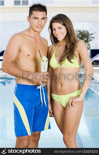 Portrait of a young man holding lemonade with a young woman standing beside him at the poolside