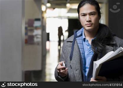 Portrait of a young man holding textbooks and a mobile phone