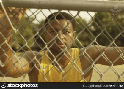 Portrait of a young man leaning against a chain-link fence