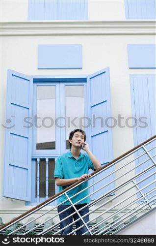 Portrait of a young man leaning against a staircase and talking on a mobile phone