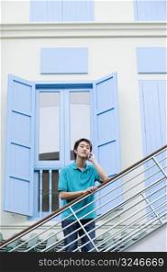 Portrait of a young man leaning against a staircase and talking on a mobile phone