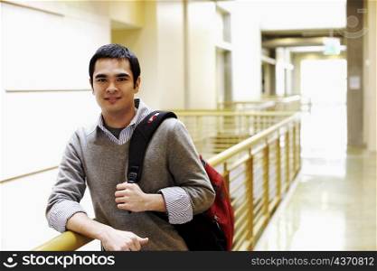 Portrait of a young man leaning against the railing of a corridor