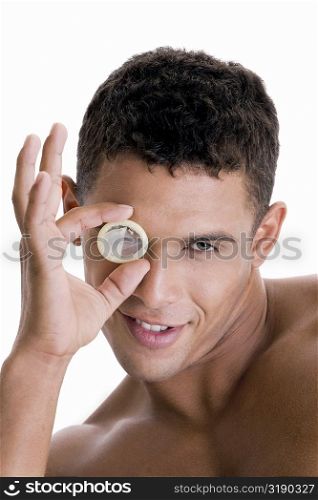 Portrait of a young man looking through a condom