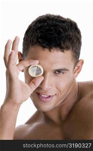 Portrait of a young man looking through a condom