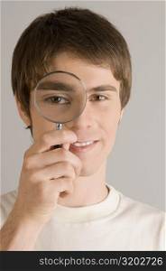 Portrait of a young man looking through a magnifying glass