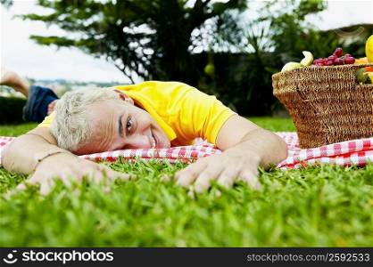 Portrait of a young man lying on a sheet in a park with a basket of fruit