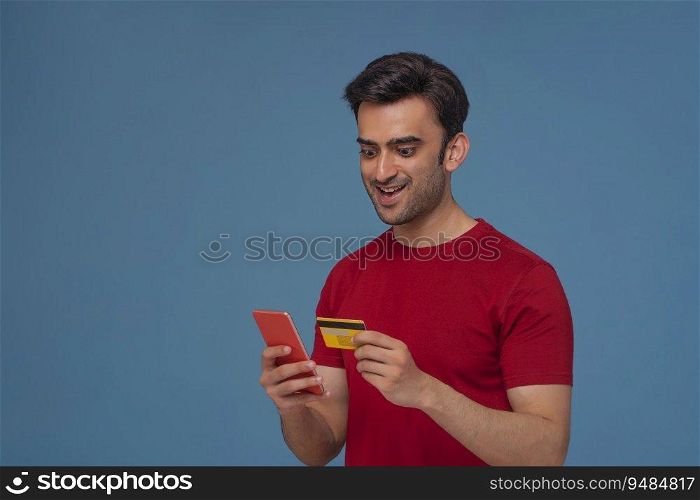 Portrait of a young man making an online transaction with credit card and mobile phone.