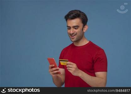 Portrait of a young man making an online transaction with credit card and mobile phone.