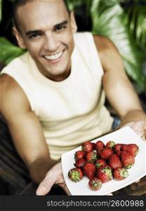 Portrait of a young man offering a plate of strawberries