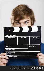 Portrait of a young man peeking behind a clapboard, over a gray background