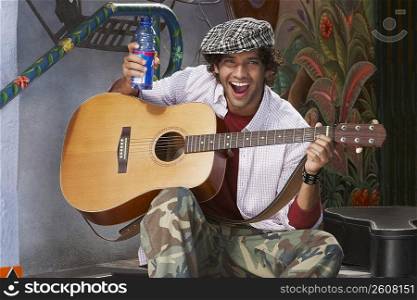 Portrait of a young man playing a guitar and holding a water bottle