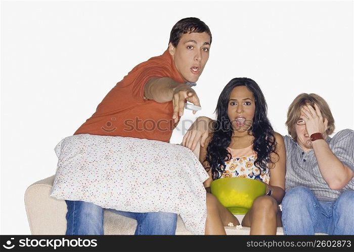 Portrait of a young man pointing forward with his two friends sitting on a couch beside him