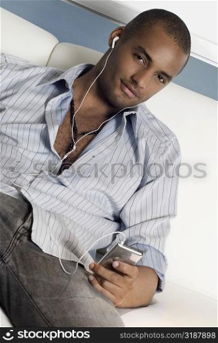 Portrait of a young man reclining on a couch and listening to an MP3 player