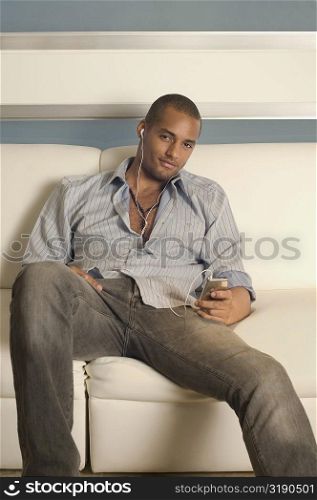 Portrait of a young man reclining on a couch and listening to an MP3 player