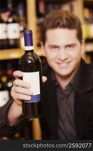 Portrait of a young man showing a wine bottle in a liquor store