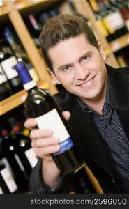 Portrait of a young man showing a wine bottle in a liquor store