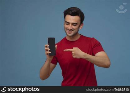 Portrait of a young man showing mobile phone in his hand against plain background.