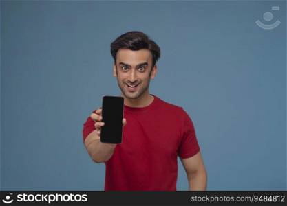Portrait of a young man showing mobile phone in his hand against plain background.