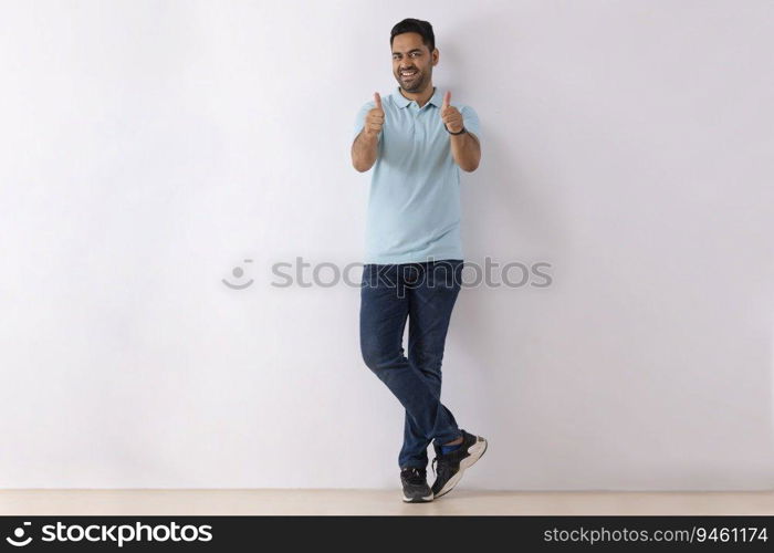 Portrait of a young man showing thumbs while standing against white background