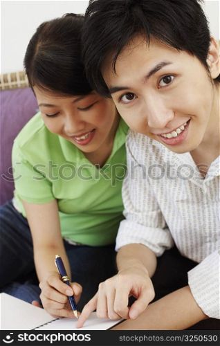 Portrait of a young man sitting and a young woman writing in a diary