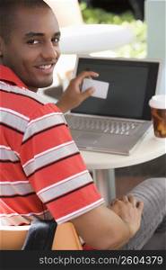 Portrait of a young man sitting at a cafe and holding a credit card