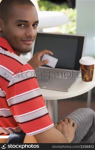 Portrait of a young man sitting at a cafe and holding a credit card