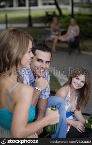 Portrait of a young man sitting between two young women and smiling