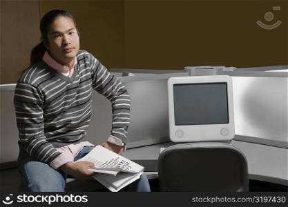 Portrait of a young man sitting in a computer lab and holding a book