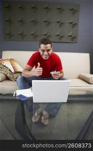 Portrait of a young man sitting in front of a laptop and showing thumbs up