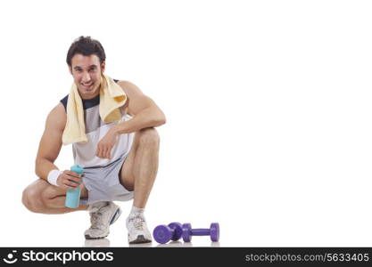 Portrait of a young man sitting next to a pair of dumbbell over white background