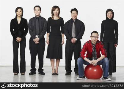 Portrait of a young man sitting on a ball with a group of business executives standing beside him