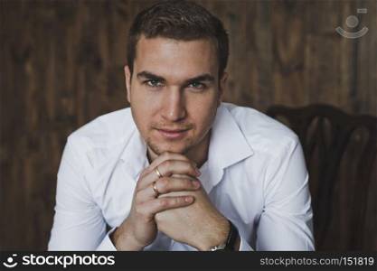 Portrait of a young man sitting on a chair.. Portrait of a man in the background of a wooden wall 6396.