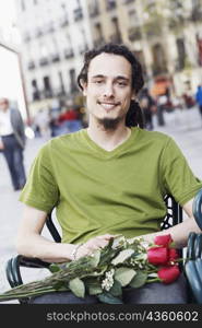 Portrait of a young man sitting on a chair with a bunch of roses on his lap