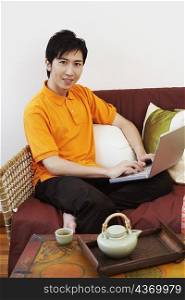 Portrait of a young man sitting on a couch and using a laptop