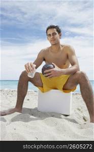 Portrait of a young man sitting on an ice box on the beach