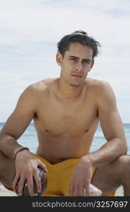 Portrait of a young man sitting on the beach and holding a soccer ball